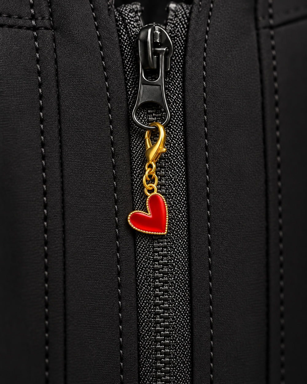 Charm AXION corazón rojo con mosquetón dorado, sujeto a un tirador de cremallera negro.