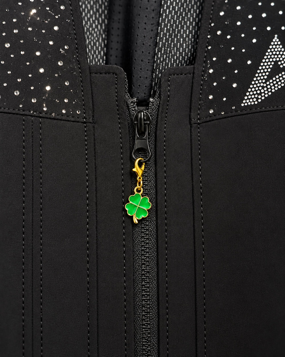 Charm AXION trébol verde con mosquetón dorado, sujeto a un tirador de cremallera negro.