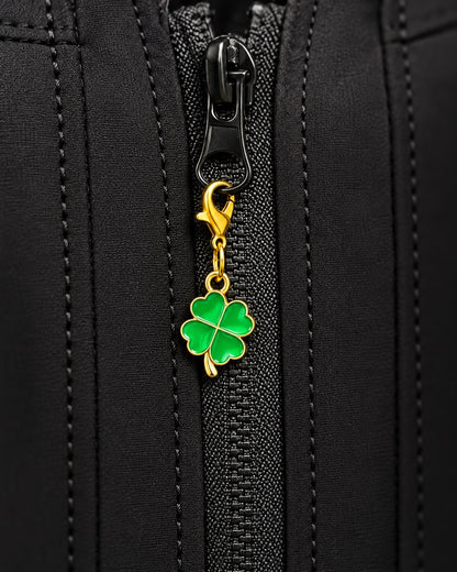 
Charm AXION quadrifoglio verde con moschettone dorato, agganciato a un tirazip nero.